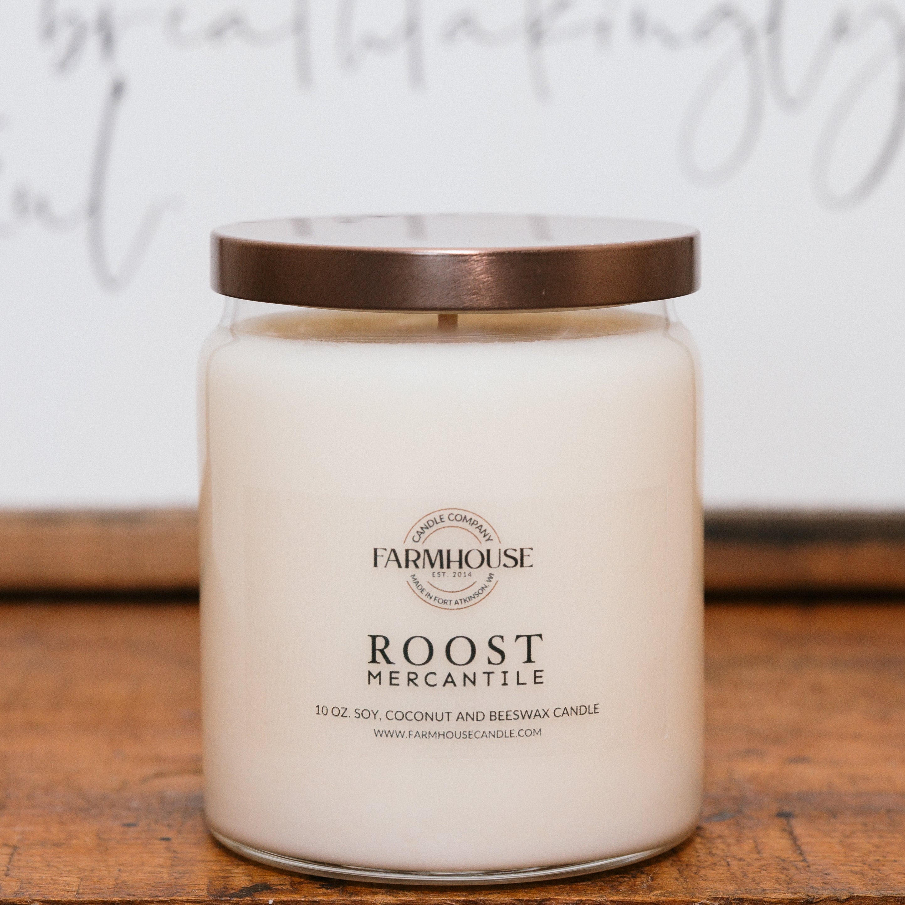 Jar candle with a brown lid on a wooden surface, featuring Farmhouse Candle Company 'Roost Mercantile' branding.