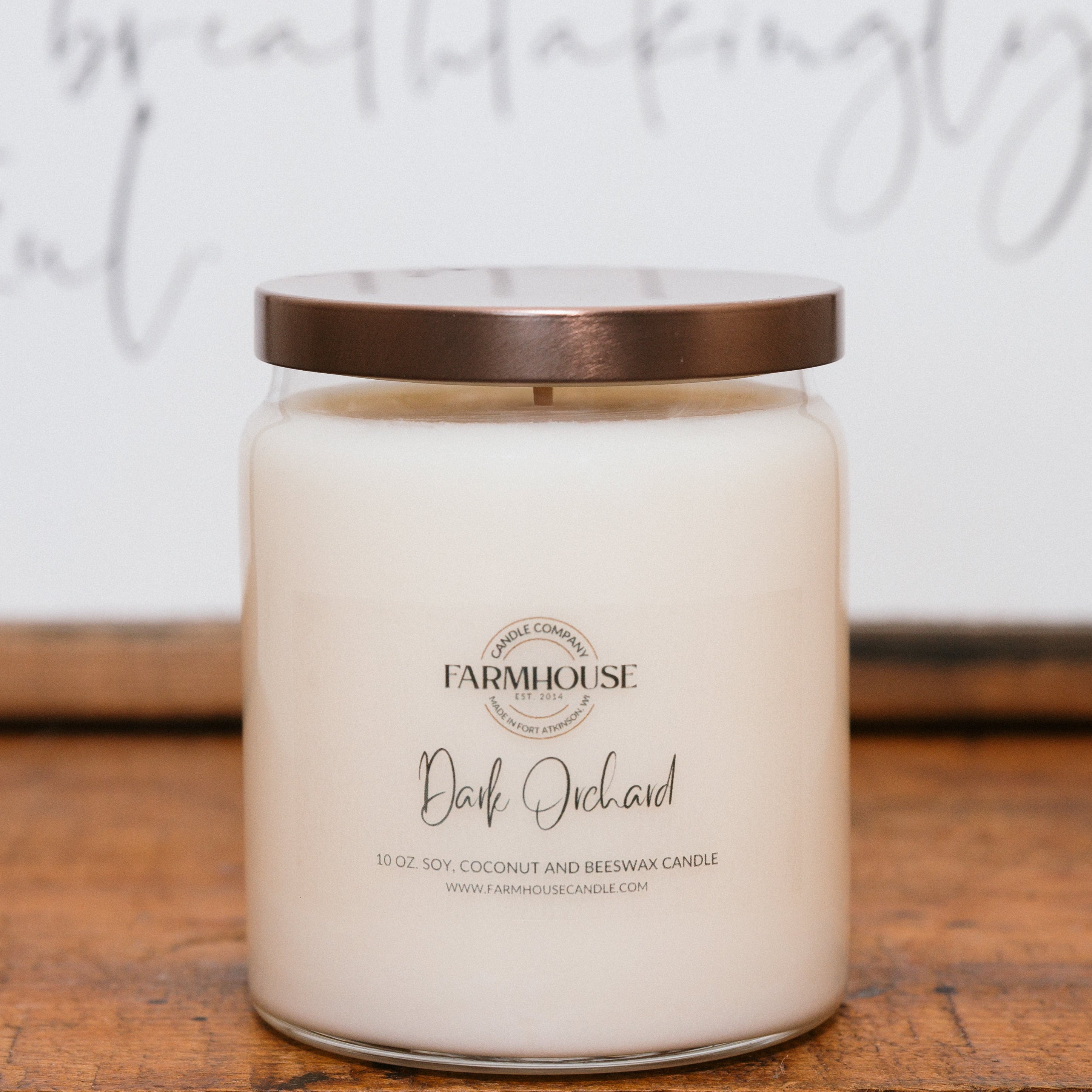 Farmhouse Candle Company candle labeled 'Dark Orchard' on a wooden surface with a blurred background.