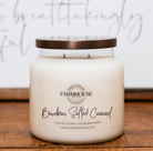 A Farmhouse Candle Company 'Bourbon Salted Caramel' soy, coconut and beeswax candle in a clear glass jar with a metallic bronze lid, resting on a wooden surface against a white background with elegant cursive writing.